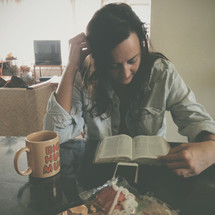 a woman sitting at a table with a cup of coffee reading a Bible 