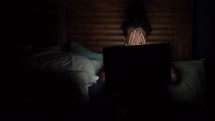 a stressed man looking at a computer at night and covering his face with his hands 