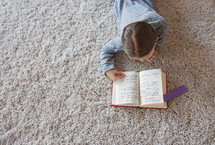 a girl reading a book on carpet 