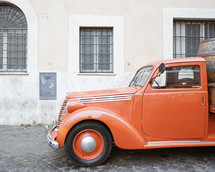 an old orange truck parked on a cobblestone street in Rome 