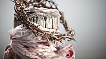 A crown of thorns and a blood-soaked garment hang from a wooden beam.