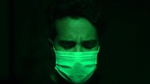 face of a man wearing a face mask in green light shaking his head no