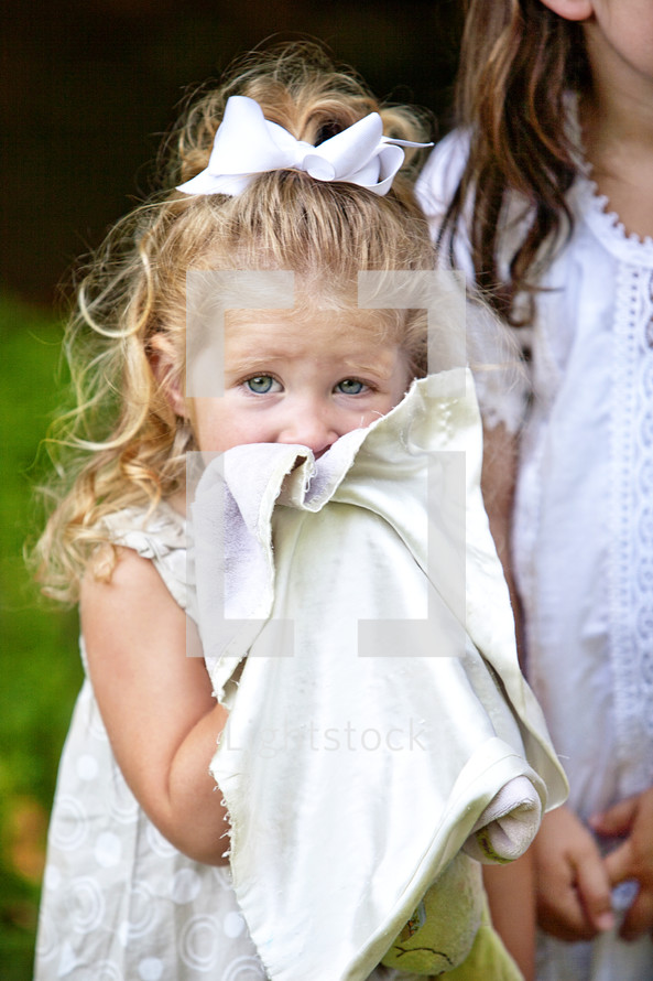 A small girl holding her blanket over her face
