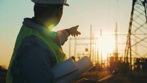 Industry energy business concept. Silhouette electrical engineer a working near tower with electricity at sunset time. Electrical worker inspect voltage electricity pylon. Power generation industry.