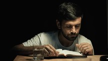 a man reading a Bible and drinking from a glass of water 