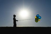 silhouette of a child holding balloons 