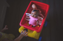 toddler pushing a babydoll in a toy shopping cart 