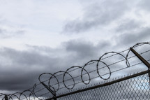 barbed wire at the top of a chain link fence under gray skies