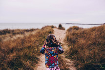 a child in a coat running towards a shore 