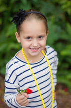 A girl wearing yellow beads holding a flower.