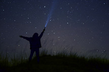 silhouette of a boy shining a flashlight into a starry night sky