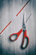 Bright red scissors cutting vibrant ribbon on wooden table, showcasing crafting creativity with touch of danger. Texture adds depth to visually appealing still life photo