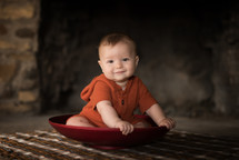 infant sitting in a bowl on a plaid blanket 