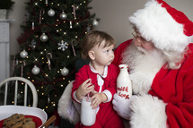 a toddler with cookies and milk sitting on Santa's lap 