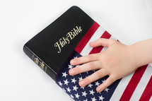 Bible draped with American flag, hand on top of the flag