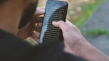 a man reading a Bible app sitting outdoors 
