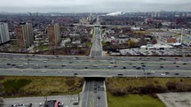 Aerial shot of a drone flying over the intersection of Highway 401 with an arterial road in Toronto on a cloudy day. The drone is moving toward a residential area right above the overpass.