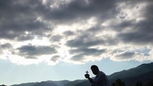 a man holding a cross praying on a mountaintop 