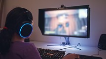 Young girl sitting in front of a computer, playing a game wearing a headset