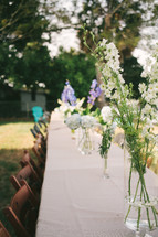 row of flowers in vases on a table at a wedding reception