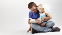 A dad reads a Bible with his young daughter in his lap.