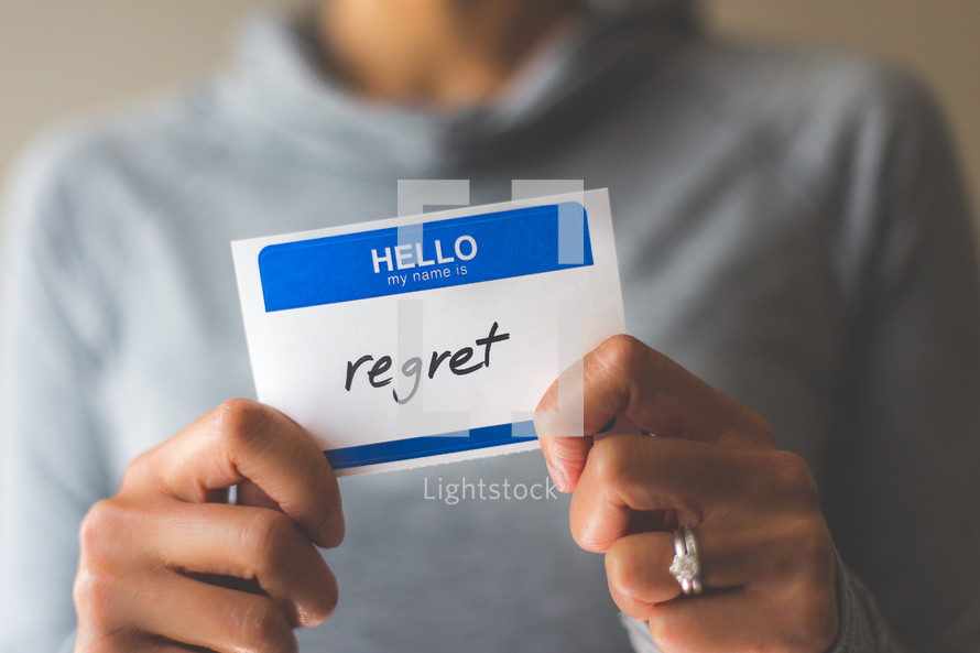 woman holding a name tag with the word regret 