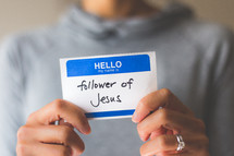 woman holding a name tag with the words follower of Jesus 