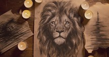 Zooming in on thick paper with charcoal drawing of a lion on it surrounded by candles