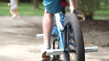 A boy rides his bike in the driveway with family play around him