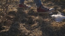 Close up of feet in converse walking on snow and grass backlit with sun rays