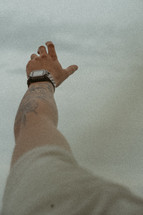 Man's arm with tattoo reaching to the sky