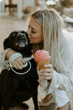 a woman holding an ice cream cone kissing a dog 