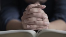 man with praying hands over a Bible 