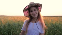 Pretty child in the wheat field. Happy young girl play in the field at sunset. Happy kid playing in the wheat field on a warm summer day at sunset.