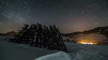 Night sky with stars moving over winter rural country with wooden frame, astronomy time lapse, dolly shot over snow
