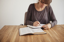 woman at a Bible study writing in a journal and reading a Bible