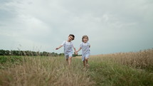 Little boys cheerfully running along path in wheat field. Children together in retro styled overall outfits. Happy brothers, freedom, childhood.