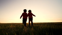 Silhouette of two little boys running together to the sun on open area field , friends holding hands. Children is our future, kids playing. Nature background. Happy childhood. High quality 4k footage