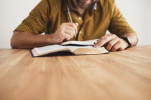 man reading a Bible and writing in a journal
