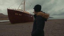 woman walking by an abandoned rusty ship 