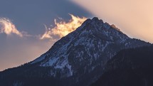 Time lapse of fast clouds motion over misty alps mountain peak in sunny winter evening nature at sunset
