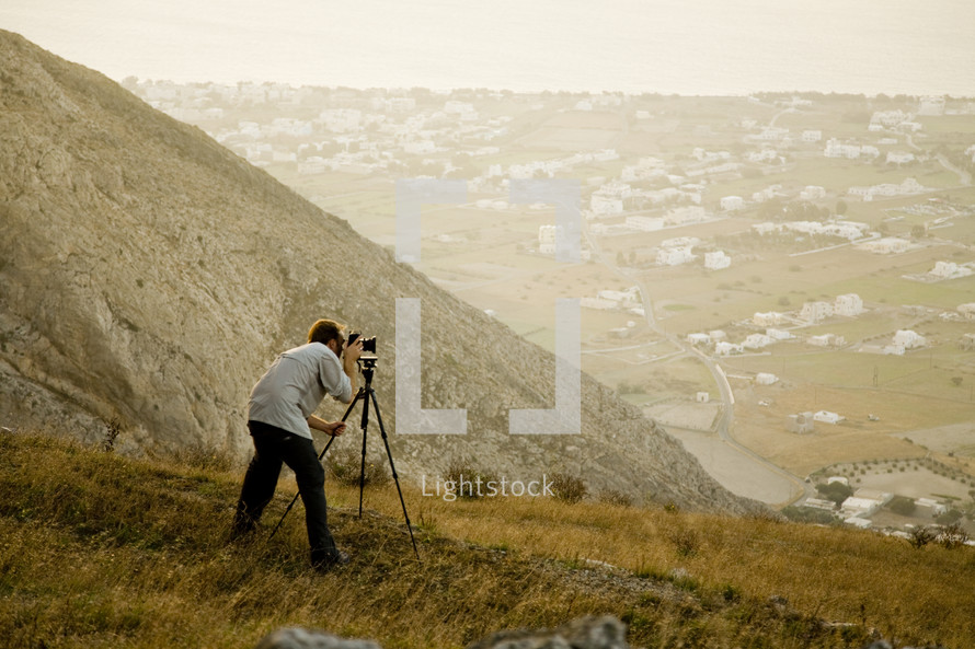A man snaps a photo using a tripod on a hillside.