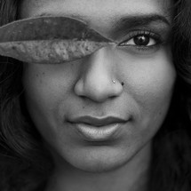 Woman holding a leaf in front of her eye.