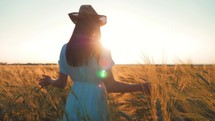 Freedom concept. Woman in a blue dress walks along a wheat field and touches spikelets of wheat with her hand in a sunset light. Free woman relax in beautiful wheat field. Wheat cultivation.