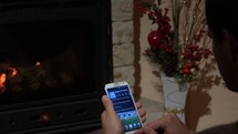 a man using a cellphone sitting in front of a fireplace 