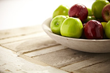 A group of green and red apples sit in a bowl