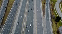 Aerial shot of a drone right above Highway 401 in Toronto on a cloudy day. The drone is tilting upwards showing a large road junction that has busy traffic. Arterial overpass over highway.
