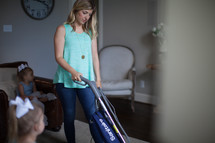 a woman vacuuming while her children watch tv 