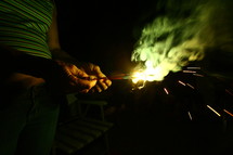 Hands holding sparklers at night.