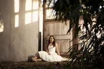 bride sitting on the ground outdoors in front of a door 